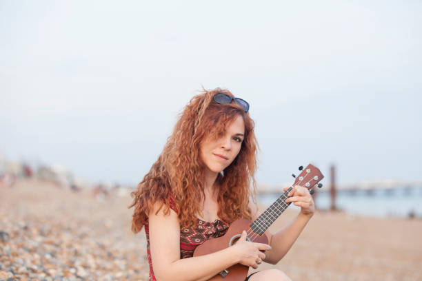 istock Young woman playing ukulele in a stone beach 694157544
