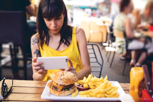 mujer fotografiando comida en restaurante - dining burger outdoors restaurant fotografías e imágenes de stock