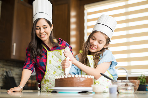 Pretty girl with a chef's hat decorating a cake she just baked with her mom at home