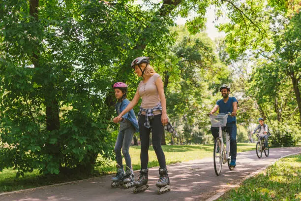 Family roller skating and riding bicycle in the public park together