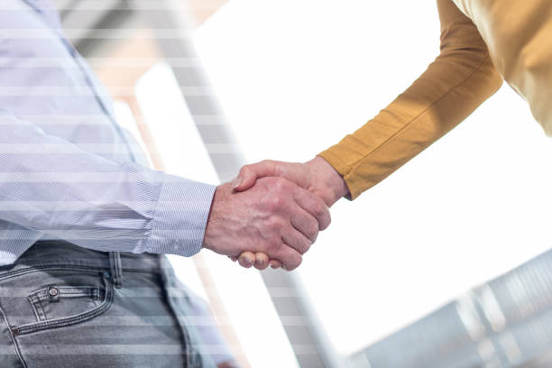istock Woman and man shaking hands in office, overlayed with rays 694204580