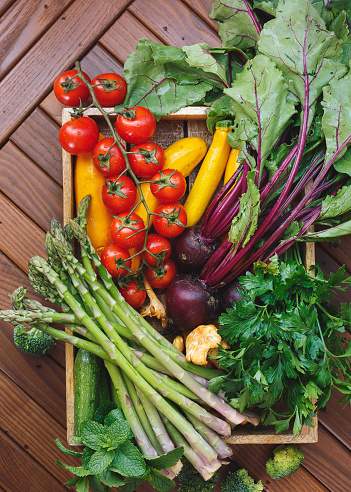 Raw fresh organic vegetables and mushrooms in rustic tray against wooden background. Top view, blank space, vintage toned image