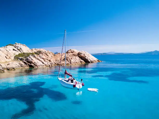 Aerial view of a sail boat in front of Mortorio island in Sardinia. Amazing beach with a turquoise and transparent sea. Emerald Coast, Sardinia, Italy."t"n