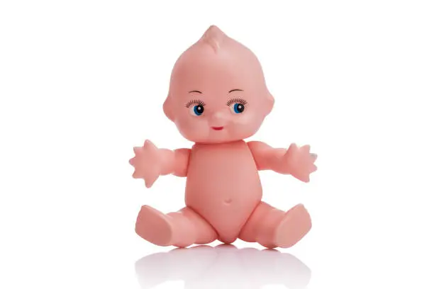 Photo of Cute little plastic baby doll with blue eyes sitting  on empty background