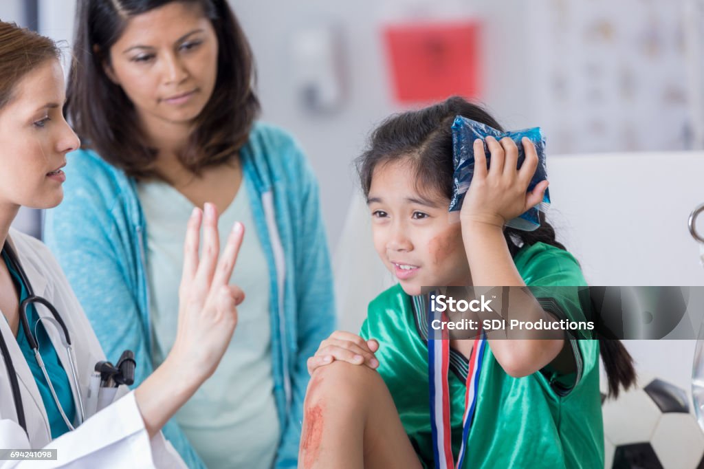 ER doctor examines dazed injured soccer player Serious female ER doctor holds up three fingers while talking with injured female elementary age soccer player. The doctor is asking the girl how many fingers she is holding up. The girl is wearing a medal and soccer uniform. Physical Injury Stock Photo