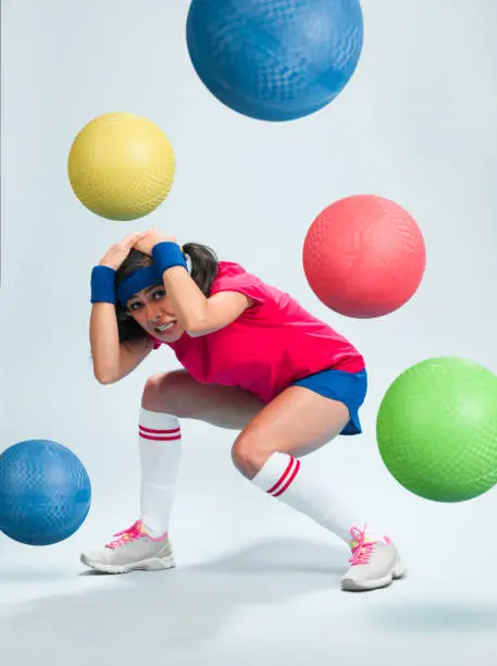 Young Hispanic Women Playing Dodgeball in a retro gym outfit with multipe balls thrown at her.