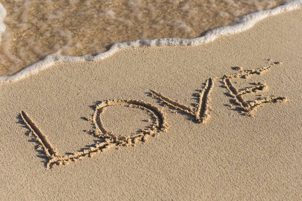 istock Inscription Love on sandy beach with wave's foam 694244922