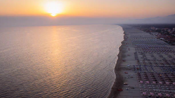 Versilia,Italy Foggy sunset over the coastline of versilia, 20 km of coast in tuscany boarded by the apuan alps and pointed by umbrellas and seats helicopter seat stock pictures, royalty-free photos & images