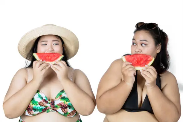 Two fat women wearing bikini, eating watermelon, isolated on white background