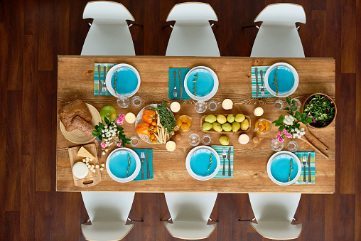 High angle view of wooden table with treats for guests and chairs around, nobody in dining room