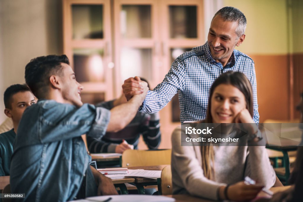 Good job, the answer is correct! Happy mid adult teacher giving a friendly handshake to teenage boy on a class. Focus is on teacher. Teacher Stock Photo