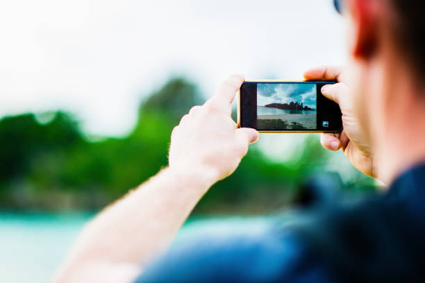 istock Man using a smartpnone with taking a photo of island 694351502