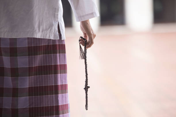Muslim man wearing islamic clothes, doing zikr while holding prayer beads