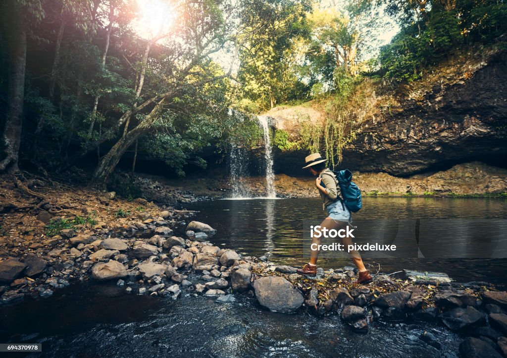 Almost there Shot of a young woman walking on a rocky surface towards a waterfall in the forest Australia Stock Photo