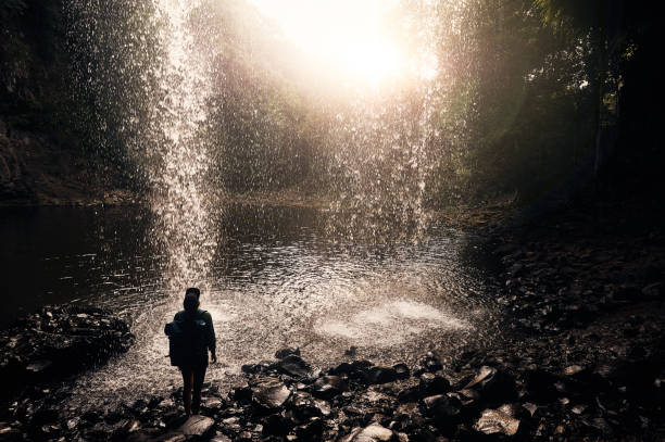 Rearview shot of a young woman enjoying the sights underneath a waterfall outdoors