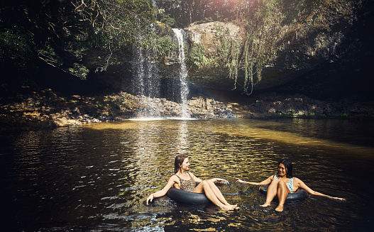 Shot of two young woman enjoying the water by a waterfall together in nature