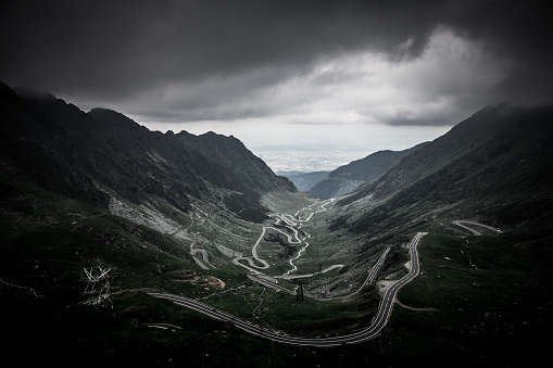 A dark and ominous sky hangs over the rugged Carpathian mountains and the Transfagarasan road that winds through this dramatic landscape in Transylvania, Romania. The Transfăgărășan or DN7C, also known as Ceaușescu's Folly, is a paved mountain road crossing the southern section of the Carpathian Mountains of Romania. It has national-road ranking and is the second-highest paved road in the country after the Transalpina.