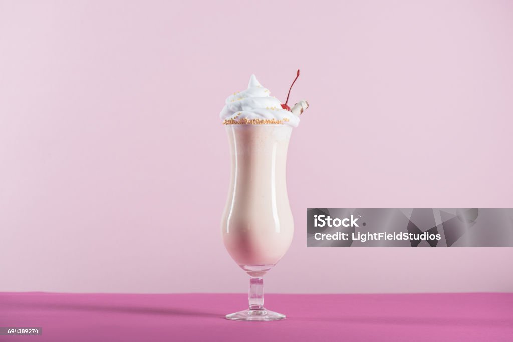 fresh milkshake with cream and cherry on top in glass on pink tabletop Milkshake Stock Photo