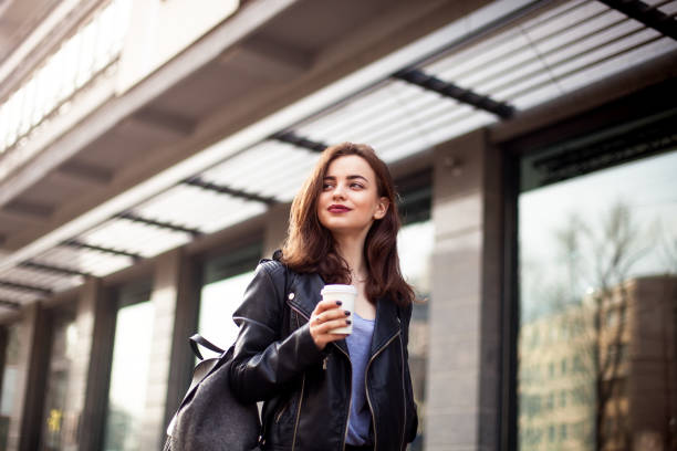 istock young beautiful brunette drinking coffee walking around the city.leather jacket,urban backpack , bright red lips 694399118