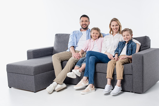Happy family with two children sitting together on couch and smiling at camera