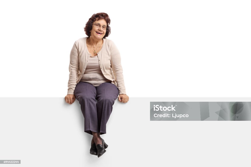 Senior woman sitting on a panel Senior woman sitting on a panel and looking at the camera isolated on white background Sitting Stock Photo