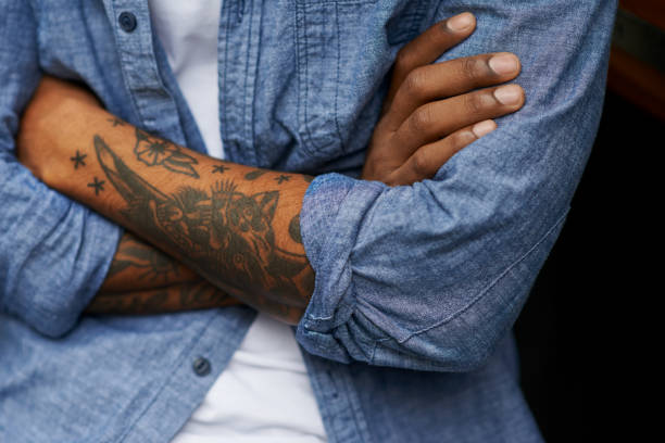 Shot of an unidentifiable man with tattoos on his arms standing outside