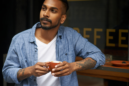 Shot of a handsome young man enjoying a cup of coffee at a cafe