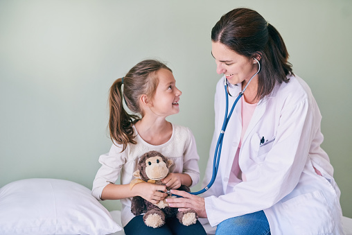 Shot of a doctor playfully holding a stethoscope against a young girl's stuffed toy