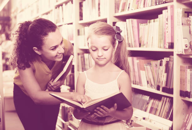 istock Female with girl  in school age looking in open book 694438580