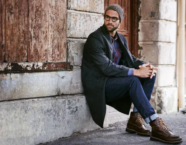 Shot of a handsome young man taking a seat on the sidewalk in the city