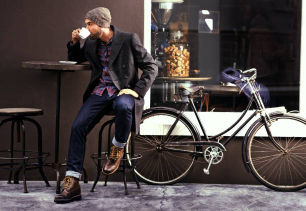 Coffee to make your day last longer Shot of a handsome young man enjoying a cup of coffee at a cafe in the city while his bike stands next to him preppy fashion stock pictures, royalty-free photos & images
