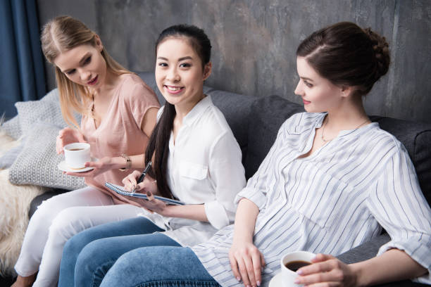 istock asian girl writing at notebook while her friends drinking coffee while sitting on sofa 694450820