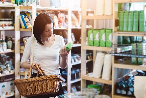 Woman choosing products in ecological shop with healthy food and reading product information on label