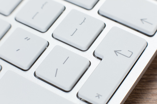 Detail of the keys on a white laptop keyboard with a top view on the enter or save button in a conceptual image