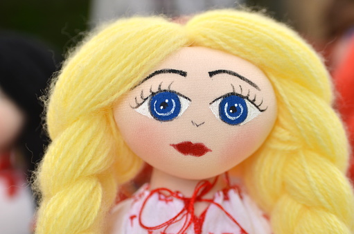 Portrait of the original handmade female doll with blond hair and big blue eyes wearing traditional Romanian clothes