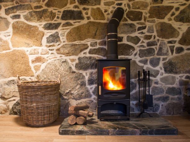 Wood Burning Stove And Fireplace The interior of a stone walled cottage with a blazing wood burner or log burning stove on a hearth with logs and storage basket. wood burning stove stock pictures, royalty-free photos & images