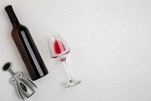 Overhead angled view of a large bottle of red wine, drinking glass on white background. Top view. Copy space