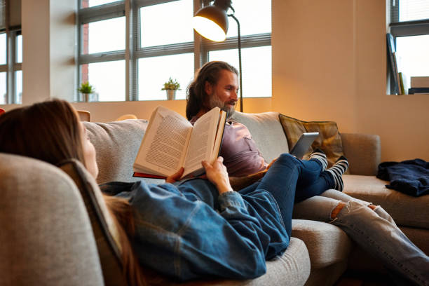 coppia matura rilassante a casa - reading book men sofa foto e immagini stock