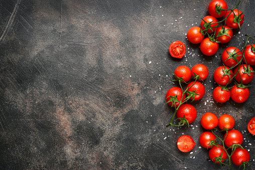 Branchs of cherry tomatoes with scattered sea salt on a rusty metal or slate background.Top view with copy space.
