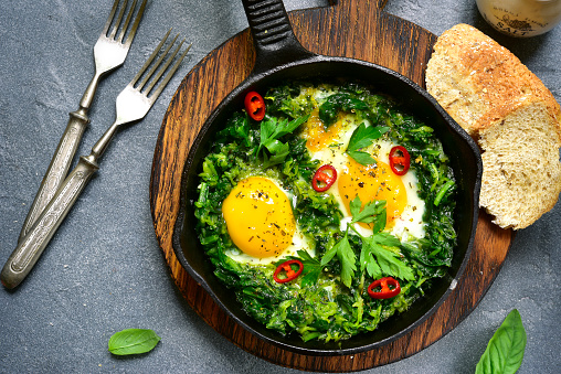 Green shakshuka in a cast iron pan on a grey slate,stone or concrete background.Top view.