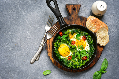 Green shakshuka in a cast iron pan on a grey slate,stone or concrete background.Top view.