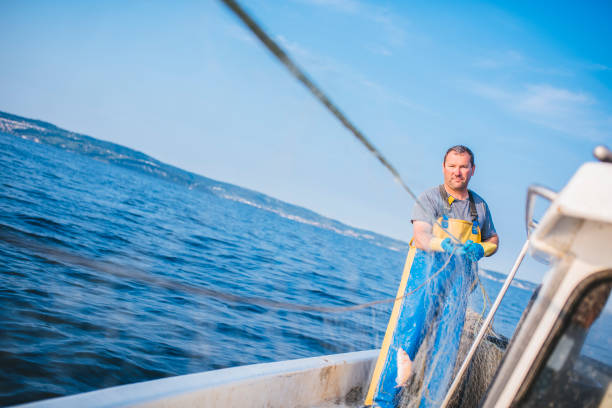 Fisherman pulling the net out of water. He is standing on his boat. Sea and blue sky in back.