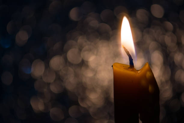 istock One candle flame light at night with bokeh on dark background 694489408