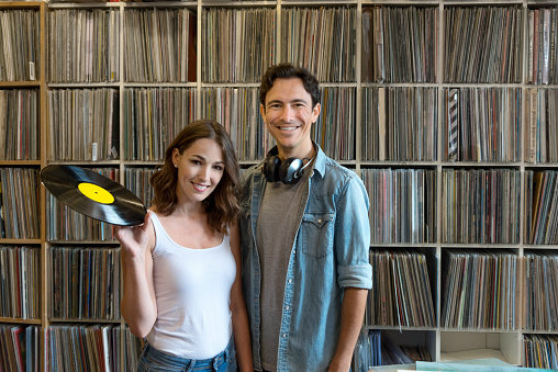 Happy couple in front of their massive record collection. He has a headset, she's holding a vinyl record.