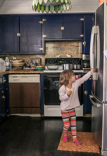 Little child opens the fridge in a domestic kitchen