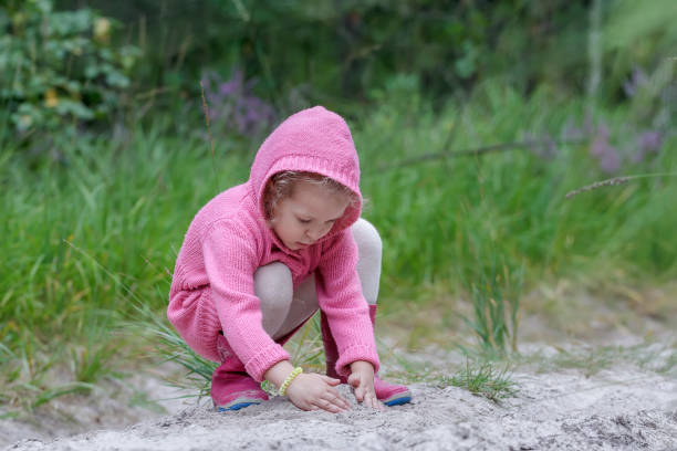 Mała dziewczynka bawi się piaskiem w letnim lesie – zdjęcie