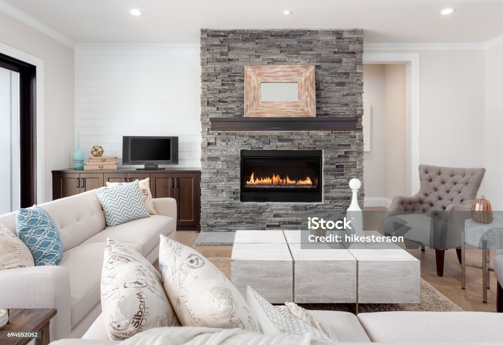 Beautiful living room interior with hardwood floors and fireplace in new luxury home. Couches at Right Angles are Opposite Armchairs and Fireplace with Surround that Stretches to Ceiling furnished living room in new home Fireplace Stock Photo