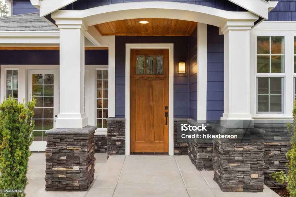 new luxury home exterior detail: patio and front door with arch and columns. Stonework graces the bottom of the columns and house while white columns and archway provide a stately welcome home exterior detail Door Stock Photo