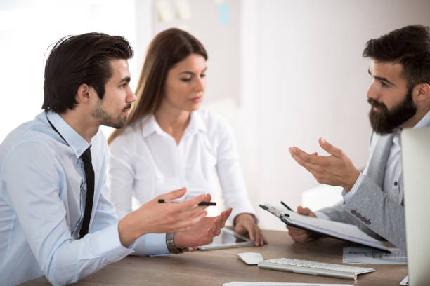 istock Team of three business people sitting at the table with several documents and discussing important questions 694563414