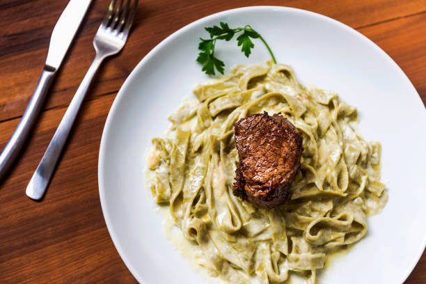 View of a green tagliatelle pasta with 4 cheese sauce and filet mignon, served on a white plate